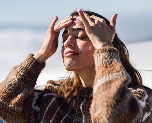 Kobieta w swetrze aplikująca krem z filtrem na twarz