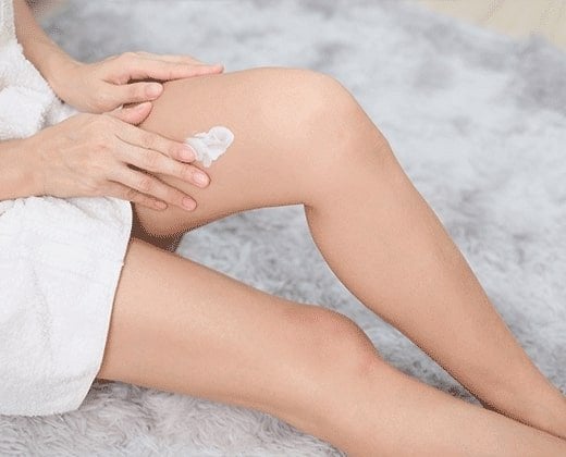Kobieta aplikuje krem na skórę nóg po krioterapii
