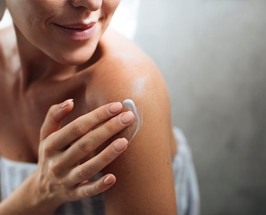 Kobieta aplikująca balsam na ramiona po kąpieli - łagodzenie objawów pokrzywki słonecznej